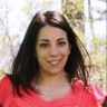 a woman in a red shirt is smiling at the camera with trees in the background