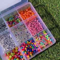 a plastic container filled with lots of different colored beads and letters on top of green grass