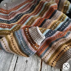 a multicolored knitted blanket laying on top of a wooden floor next to a cell phone