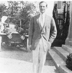 an old photo of a man in a suit and tie standing on the steps next to a car