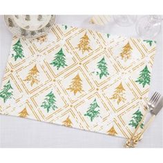 a place mat with christmas trees on it next to silverware and wineglasses