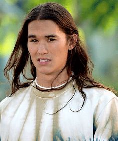 a young man with long hair wearing a tie dye shirt and looking at the camera