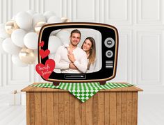 a man and woman are hugging on an old tv set with balloons in the background