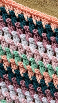 a crocheted blanket is laying on a wooden table with a piece of wood in the background