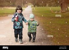 two young children walking down a dirt road in the rain - stock image, with trees and