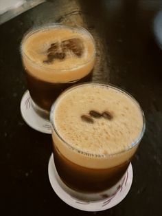 two glasses of coffee sitting on top of a table next to each other with the same liquid in them