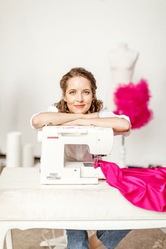 a woman sitting at a sewing machine with her arms on the table and looking into the camera