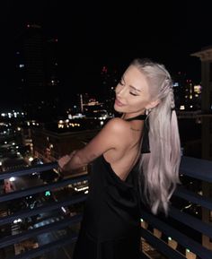 a woman with long hair standing on top of a balcony next to a city at night