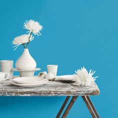 a table topped with white vases and cups filled with flowers on top of a wooden table