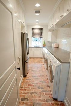 a narrow kitchen with white cabinets and brick flooring, along with a washer and dryer