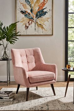 a pink chair sitting in front of a window next to a table with a potted plant