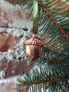 an ornament hanging from a pine tree with snow on the ground and brick wall behind it