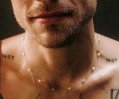 a close up of a man with tattoos on his arm and chest, wearing a pearl necklace