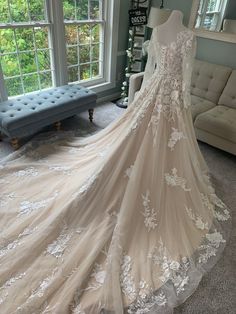 a wedding dress on display in front of a window with a couch and windowsill