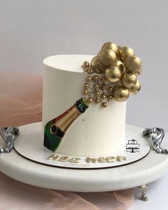 a white cake with gold decorations and a champagne bottle on top, sitting on a plate