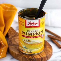 a can of pumpkin puree on a wooden board with cinnamon sticks in the background