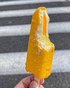 a person holding an orange popsicle with cream on it