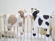 two crocheted cows standing next to each other in a crib with stuffed animals