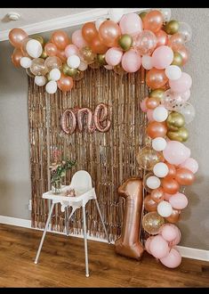 a balloon arch with the number one on it in front of a chair and table