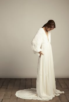 a woman in a long white dress standing on a wooden floor with her back to the camera