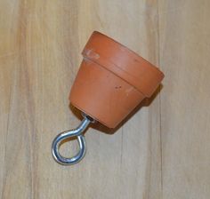 a small brown pot with a metal hook attached to it on a wooden table top