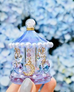 a hand holding a small blue bell with pearls on it's sides and a gold chain around the bell