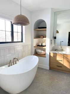 a large white bath tub sitting in a bathroom next to a sink and window with open shelves