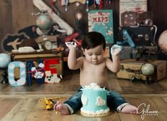 a young boy sitting on the floor with a cake in front of him and his hands up