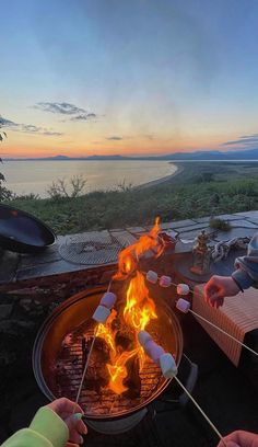 two people roasting marshmallows over an open fire pit at the beach