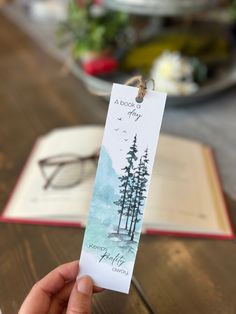 a person holding up a bookmark with trees on it