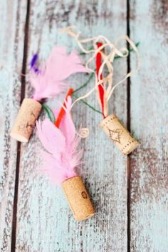 some wine corks with pink feathers and twine on them sitting on a wooden table