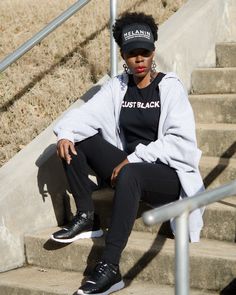 a woman sitting on the steps wearing a black hat and sweat shirt with just black written on it