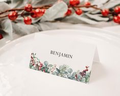 a place card sitting on top of a white plate with berries and leaves around it