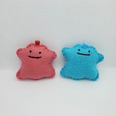 two small stuffed animals sitting next to each other on a white surface, one is blue and the other is pink