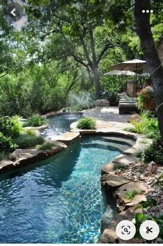 an outdoor swimming pool surrounded by lush green trees and rocks, next to a patio with umbrellas