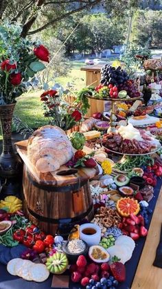 a table filled with lots of food on top of a wooden barrel next to a tree