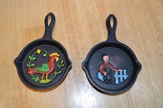 two cast iron frying pans with painted images on them