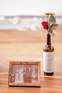 a wine bottle with a red rose in it next to an old photo frame on a table