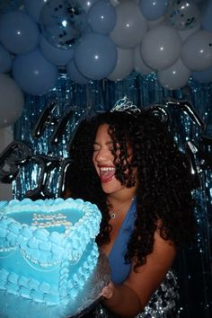 a woman holding a blue cake in front of balloons