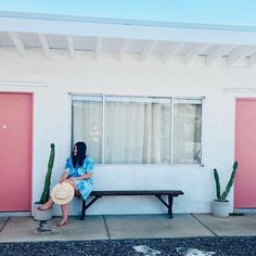 a woman sitting on a bench in front of a building with pink doors and cactus