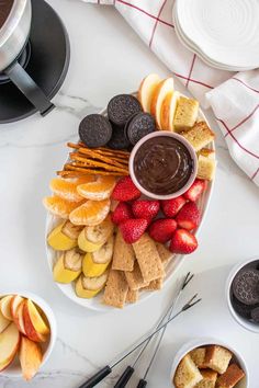 a platter filled with fruit, crackers and chocolate sauce on top of a white table