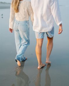 a man and woman walking on the beach holding hands with each other's legs