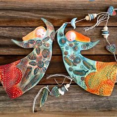 two colorful ceramic birds sitting on top of a wooden table next to beads and necklaces