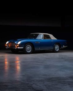 an old blue sports car parked in a dark room with its hood up and lights on