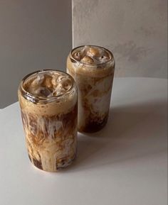 two glasses filled with iced coffee sitting on top of a white table next to each other