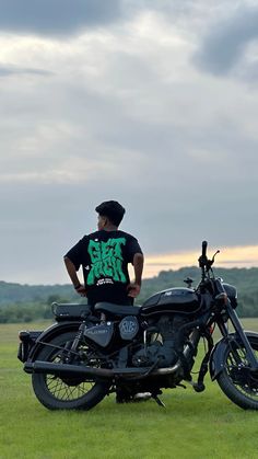 a man standing next to a motorcycle on top of a lush green field under a cloudy sky