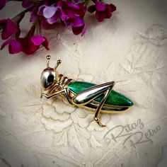 Stunning cricket brooch with 18ct gold plated body and glossy green enamel body with black enamel eyes. It is very attractive and well made.  The piece has a roll-over safety catch.   This beautiful brooch, by the costume jewellery company Cabouchon, is in very good pre-loved condition.  The last pic shows an original Cabouchon info leaflet confirming the quality of their jewellery.  Size: H 25mm x W 50mm Comes boxed and shipped by Royal Mail tracked service. Leaflet not included. CABOUCHON Jewe Formal Green Enamel Brooches, Elegant Green Enamel Pin, Green Bug, Insect Brooch, Frog Pins, High Society, Green Enamel, Jewelry Companies, Black Enamel