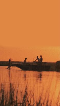 some people are riding in a boat on the water at sunset or dawn, with tall grass and reeds