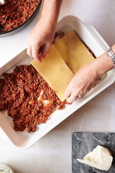 a person is spreading cheese on top of some food in a casserole dish