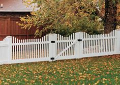 a white picket fence in front of a house with autumn leaves on the grass and trees